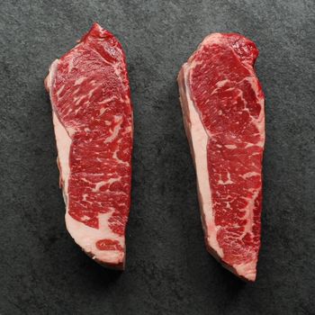 overhead view of two raw, 16 oz new york strip steaks