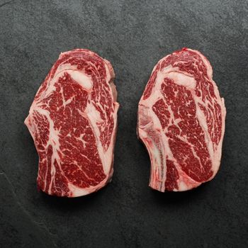 overhead view of two well-marbled bone-in, raw rib steaks