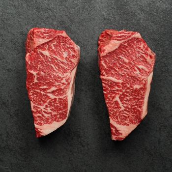 overhead view of two richly marbled raw 16 oz new york strip steaks