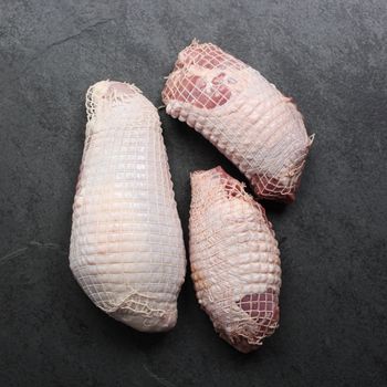 overhead view of a raw netted turkey breast and two raw netted turkey thighs