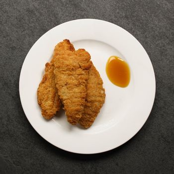 overhead view of cooked golden-brown, crispy chicken fingers on a plate with dipping sauce