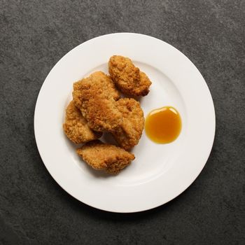 overhead view of cooked, golden-brown crispy breaded chicken bites on a plate with dipping sauce