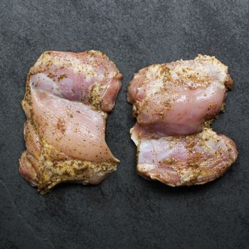overhead image of 2 raw, boneless, skinless chicken thighs lightly coated in a greek marinade