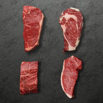 Overhead view of four different raw steaks, 1 flat iron steak, 1 rib eye steak, & 2 New York Steaks