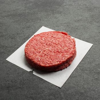 angled view of a raw wagyu beef chuck brisket burger on a piece of parchment paper