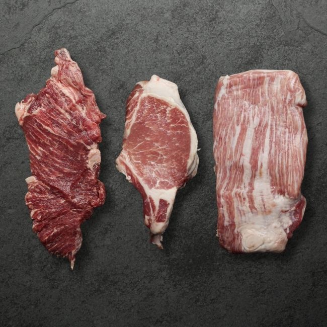 overhead image of three raw, heavily marbled cuts of Spanish Iberico Pork.