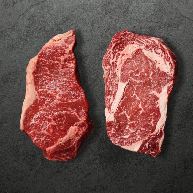 overhead view of a raw New York steak and a raw rib eye steak