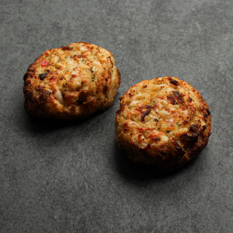 Side angle image of two cooked Seafood & Crab Cakes on a slate.