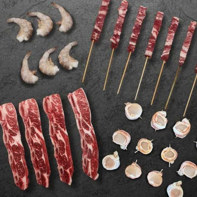 overhead view of raw miami chuck short ribs, lamb spiedini, white shrimp, and bacon-wrapped scallops