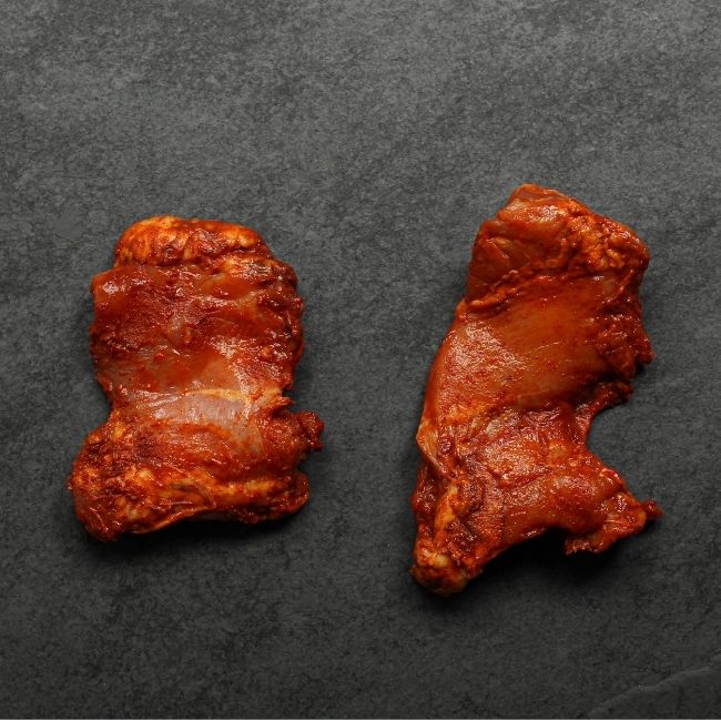 overhead view of two raw boneless skinless chicken thighs coated in a sweet bbq glaze