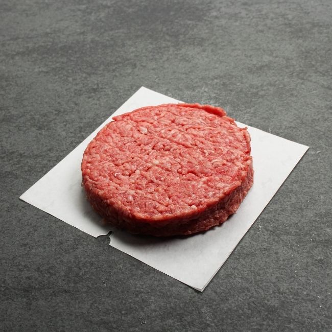 angled view of a raw wagyu beef chuck brisket burger on a piece of parchment paper