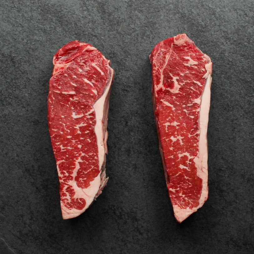 overhead view of two raw, 16 oz new york strip steaks