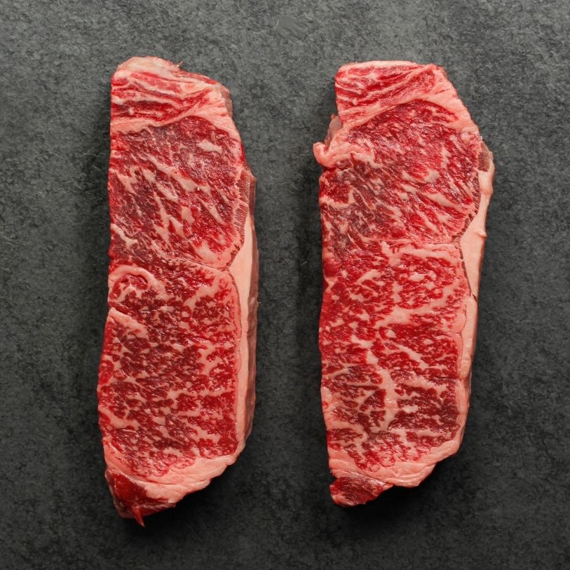 overhead view of two raw, heavily marbled Australian wagyu beef New York steaks