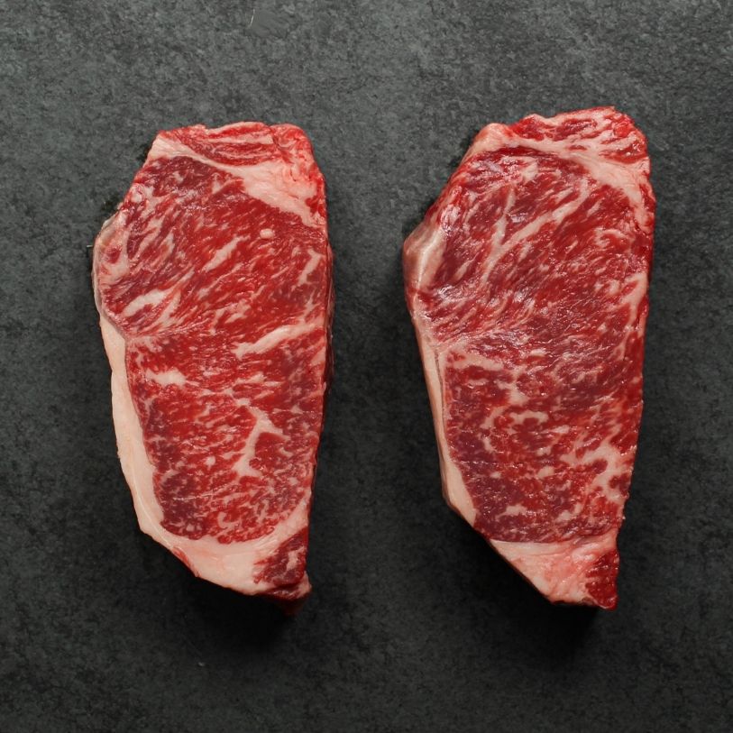 overhead view of two richly marbled raw 16 oz new york strip steaks