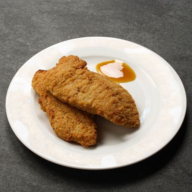 angled view of cooked golden-brown, crispy chicken fingers on a plate with dipping sauce
