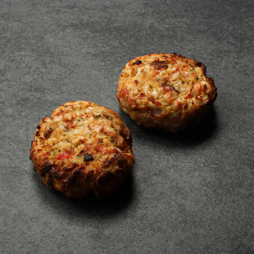 Side angle image of two cooked Seafood & Crab Cakes on a slate.