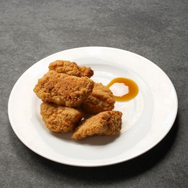 angled view of cooked, golden-brown crispy breaded chicken bites on a plate with dipping sauce