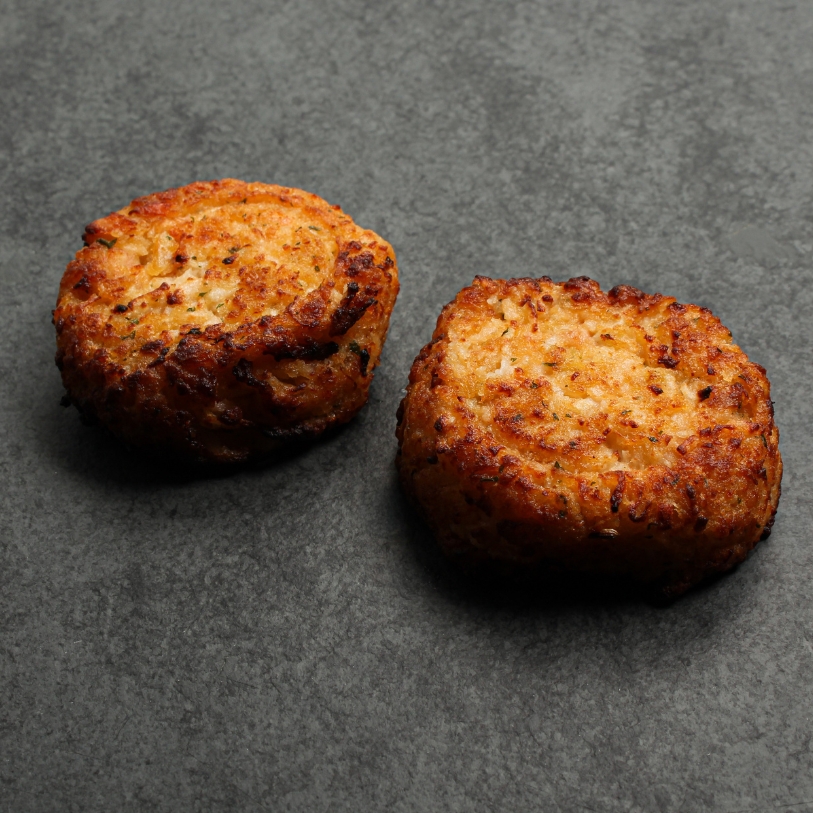 Side angle image of two cooked Lobster & Seafood cakes on a slate.