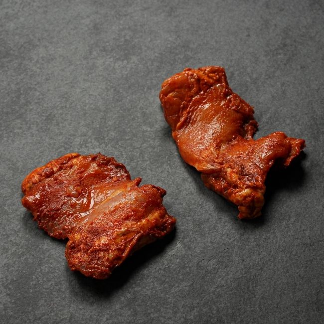 angled view of two raw boneless skinless chicken thighs coated in a sweet bbq glaze