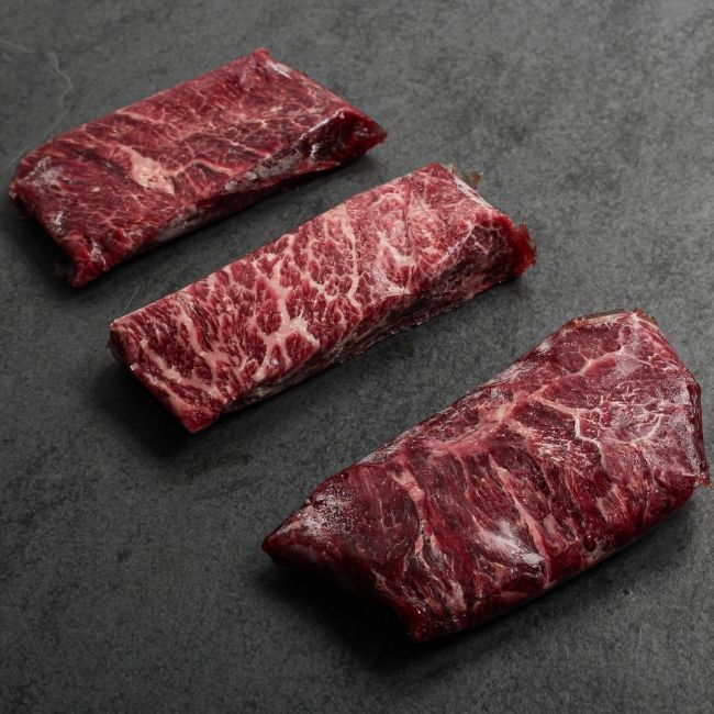 angled view of three raw American wagyu beef flat iron steak random portions