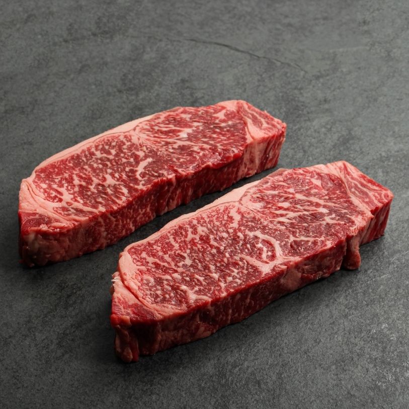 angled view of two raw, heavily marbled Australian wagyu beef New York steaks