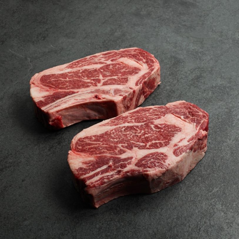 angled view of two well-marbled bone-in, raw rib steaks