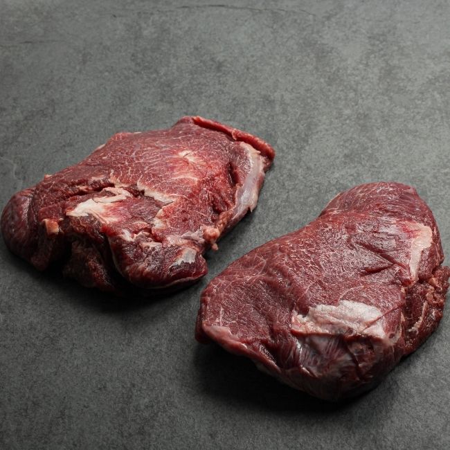 angled view of two raw, richly-marbled beef cheeks