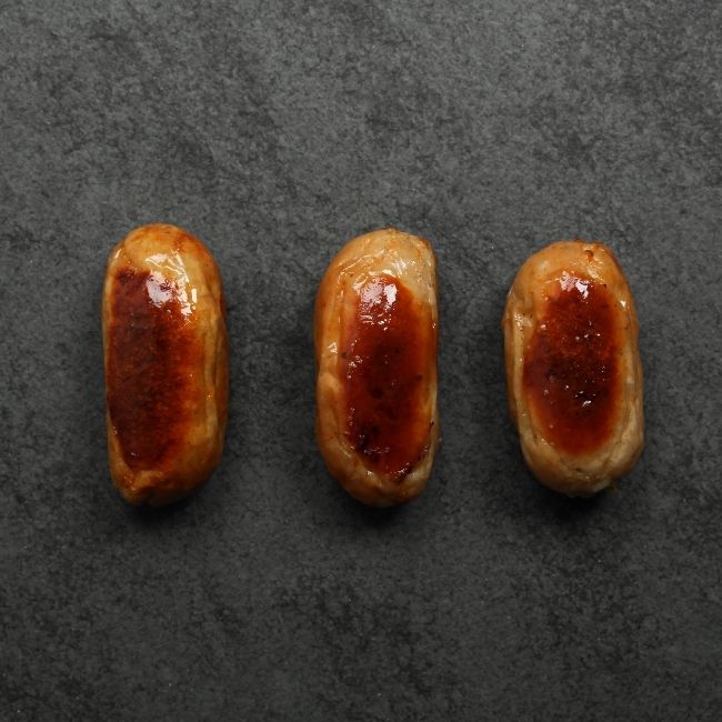 overhead view of 3 cooked classic English breakfast banger sausages on a white plate