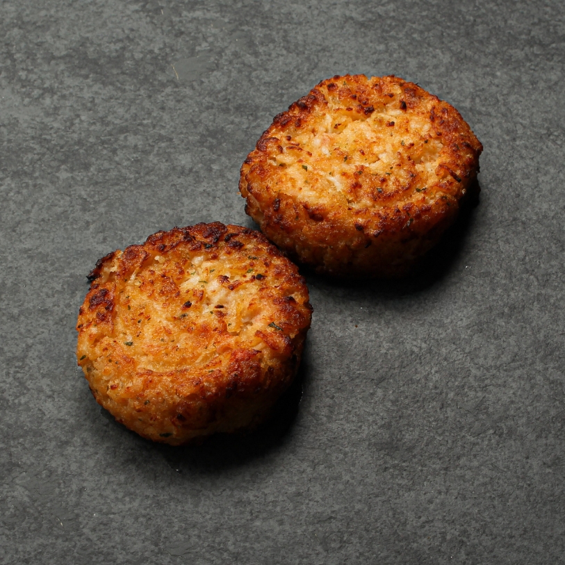 Side angle image of two cooked Lobster & Seafood cakes on a slate.