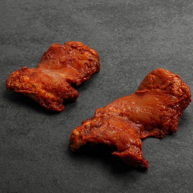 angled view of two raw boneless skinless chicken thighs coated in a sweet bbq glaze