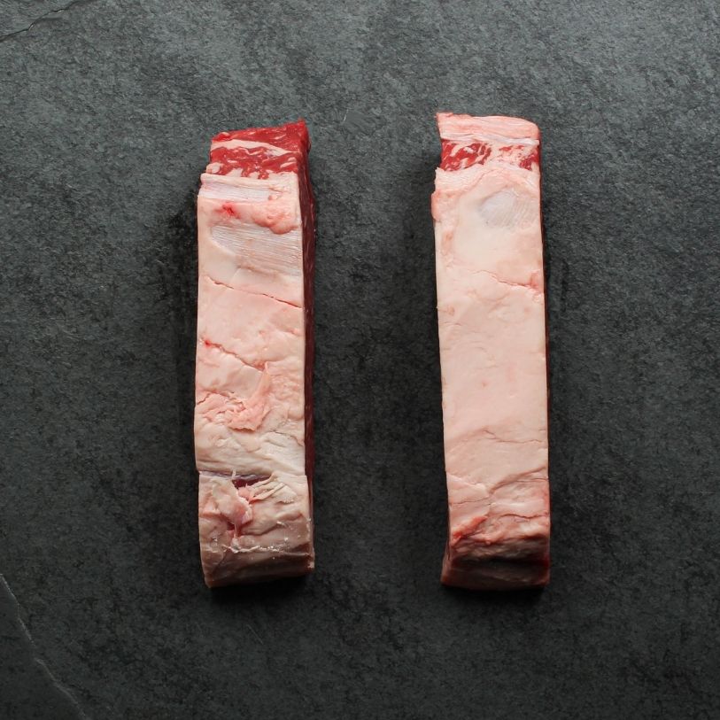 side view of two raw, 16 oz new york strip steaks