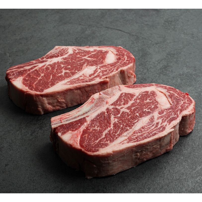 angled view of two well-marbled bone-in, raw rib steaks