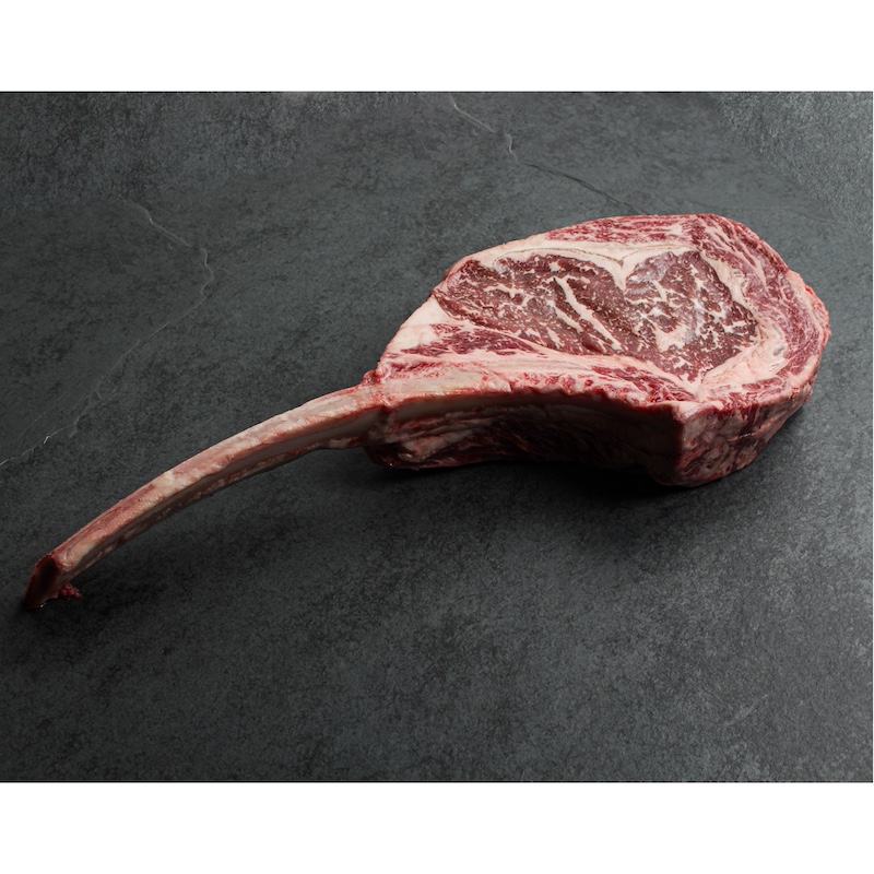 angled view of a raw, richly-marbled wagyu beef tomahawk steak