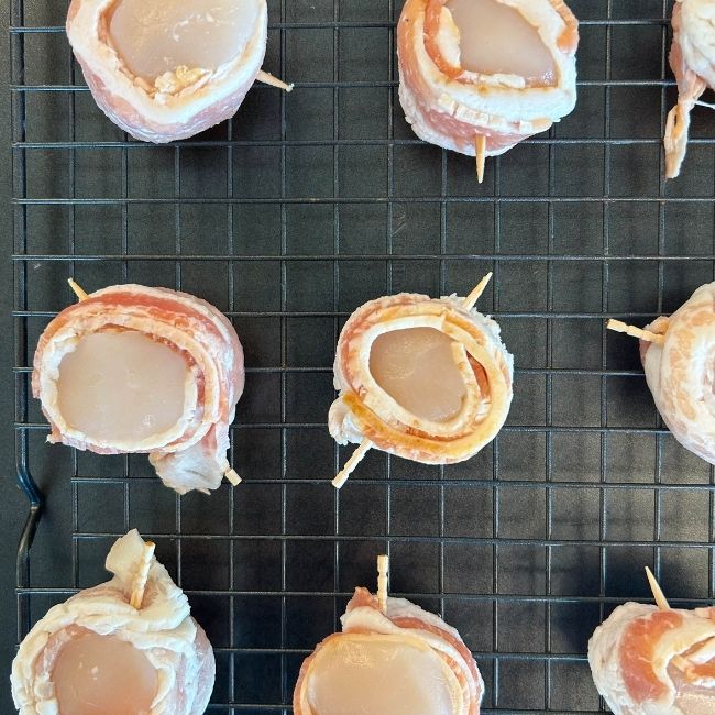 overhead view raw toothpick-skewed bacon-wrapped scallops on a wire rack-lined nonstick baking sheet