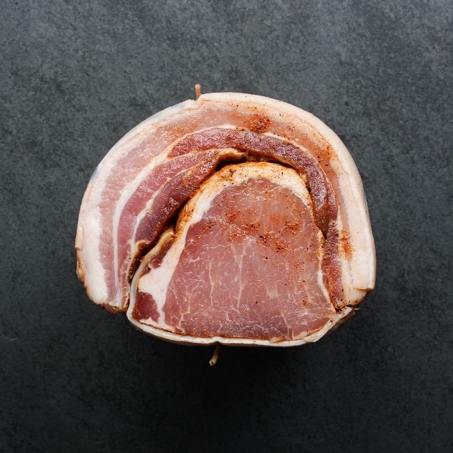 side view of a raw, seasoned and tied porchetta roast
