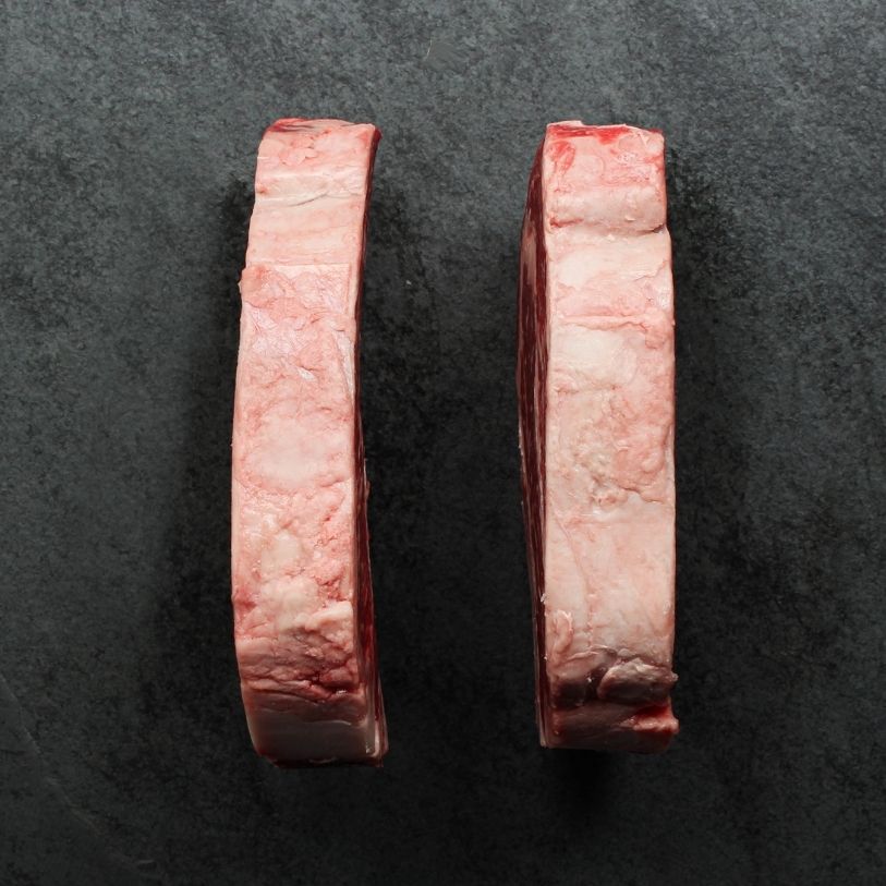 overhead view of the sides of two well-marbled bone-in, raw rib steaks