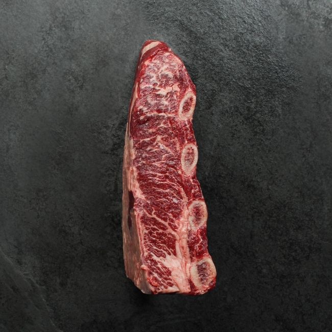 side view of a piece of raw beef short ribs with 4 bones