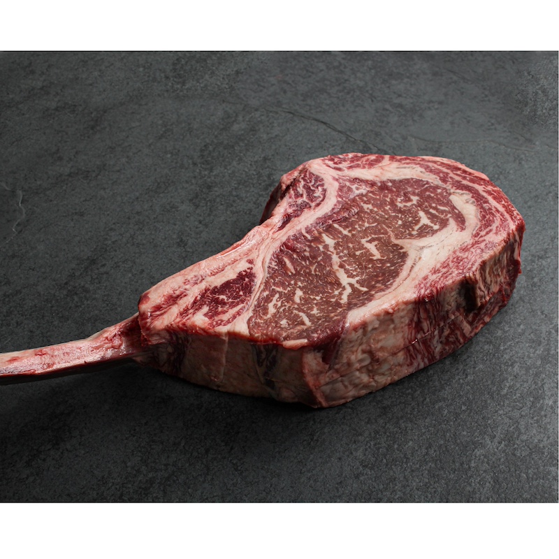 angled view of a close-up of a raw, richly-marbled wagyu beef tomahawk steak