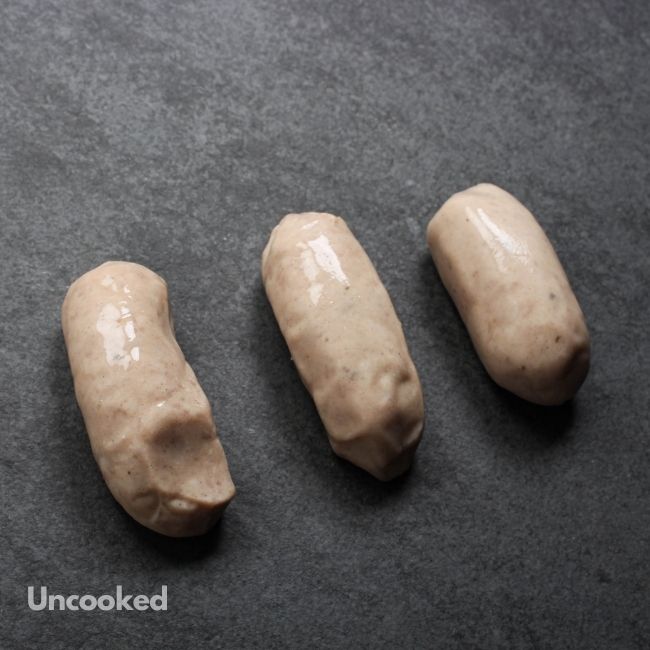 angled view of 3 uncooked classic English breakfast banger sausages