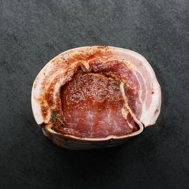 side view of a raw, seasoned and tied porchetta roast