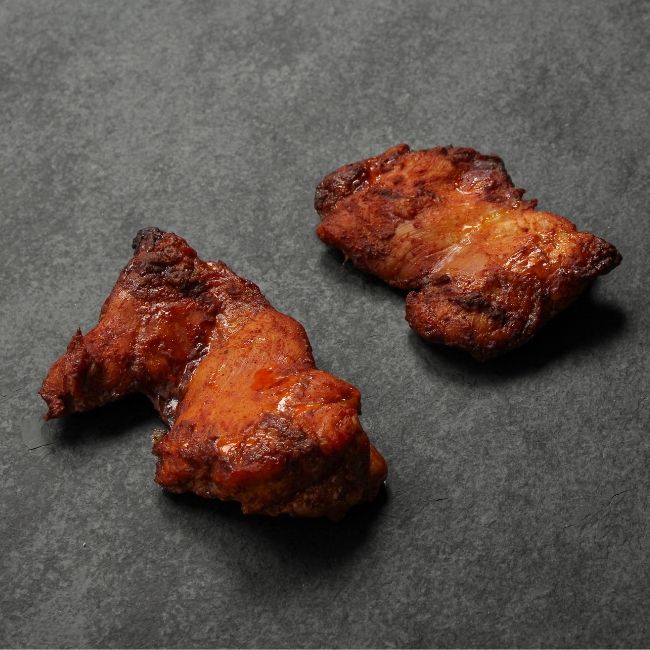 angled view of two cooked boneless skinless chicken thighs coated in a sweet bbq glaze