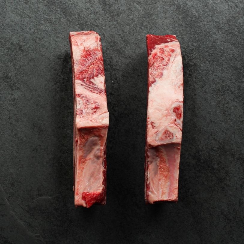overhead view of the sides of two well-marbled bone-in, raw rib steaks