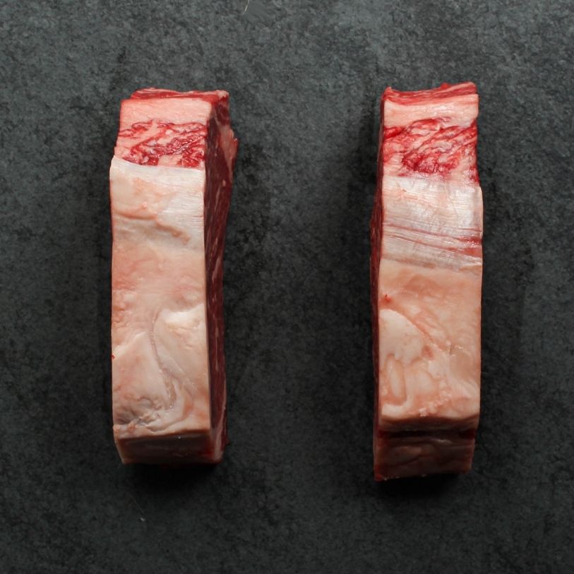 side view of two richly marbled raw 16 oz new york strip steaks