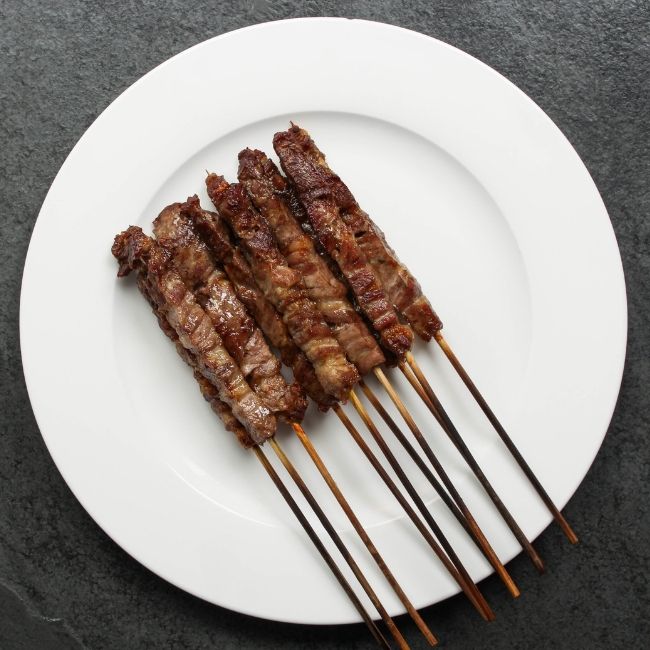 overhead view of cooked and browned mini lamb skewers on a white plate