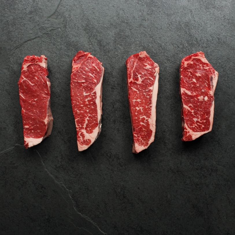overhead view of four raw, 16 oz new york strip steaks