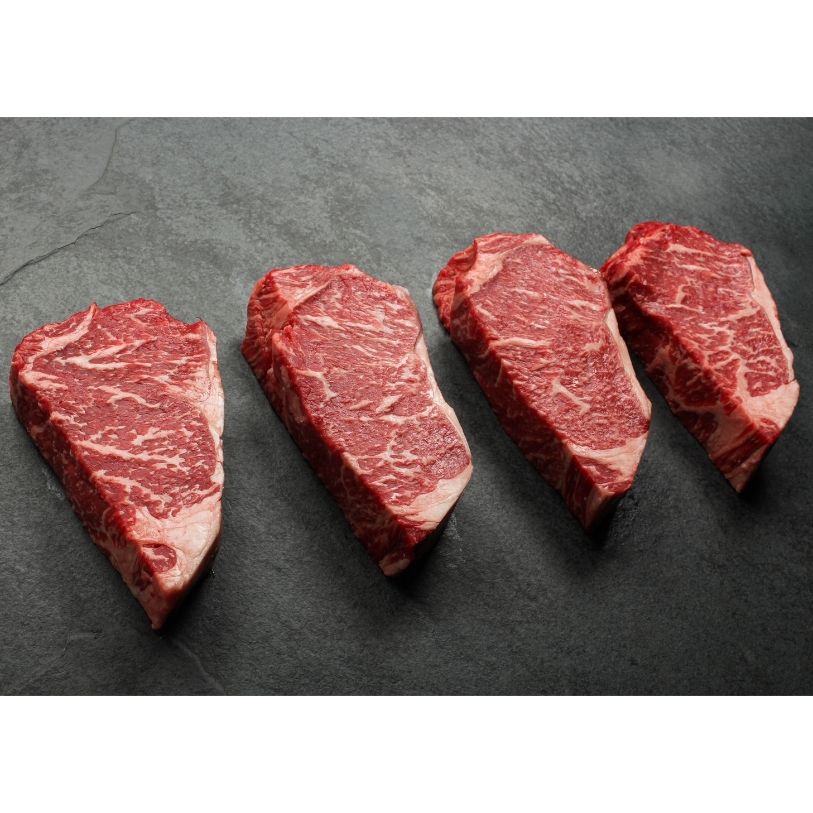angled view of four richly marbled raw 16 oz new york strip steaks