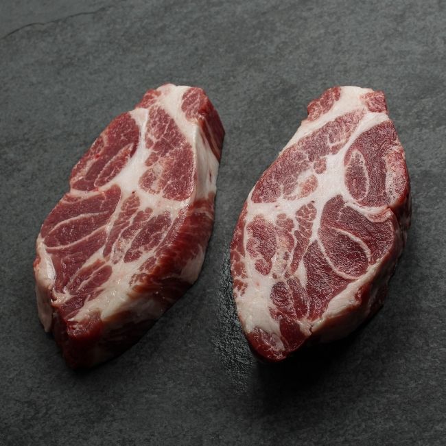 angled view of two heavily marbled iberico pork collar steaks
