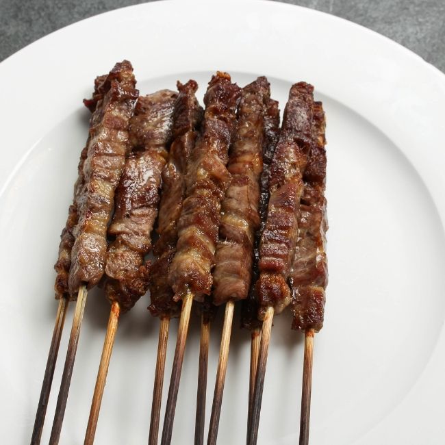angled view of cooked and browned mini lamb skewers on a white plate