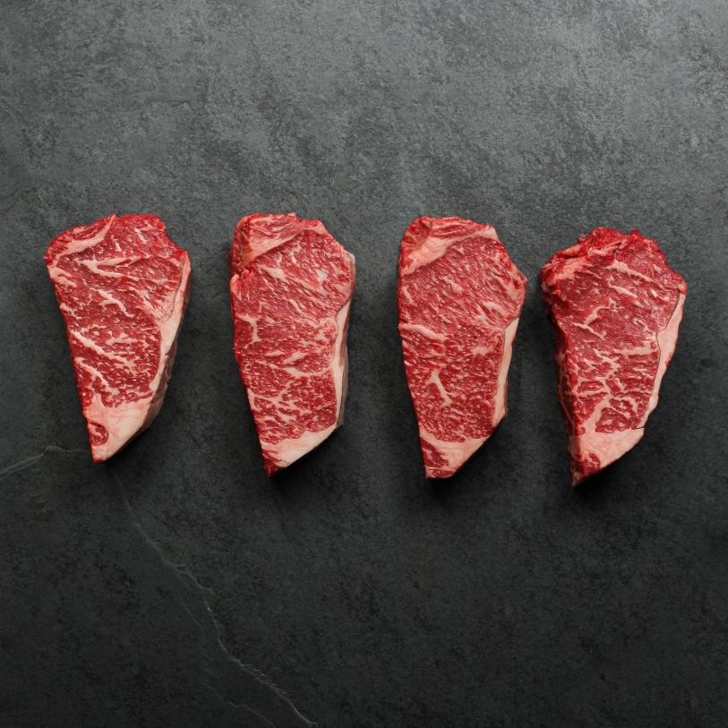 overhead view of four richly marbled raw 16 oz new york strip steaks